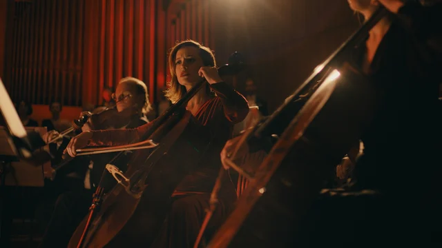 orkiestra w słabym świetle scenicznym, wiolonczelistka patrzy zaniepokojona przed siebie